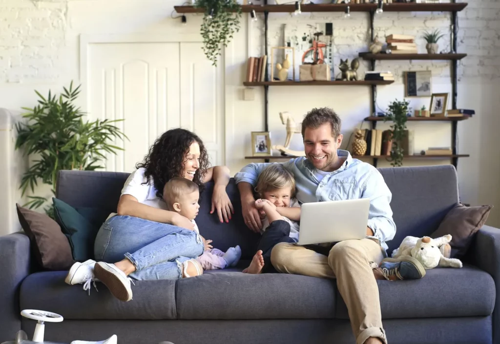 Happy family, mom, dad, children in couch with laptop computer. Compare light plans, switch and save up to thousands. EnerWisely smart app, TXU Energy