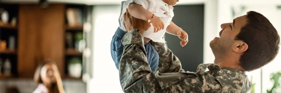 Happy Military family, veteran dad with baby, mom in the background. Compare light plans, switch and save up to thousands. EnerWisely smart app, Veteran Energy Texas