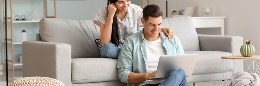 Picture, happy young couple sitting on couch looking at laptop. Texas electricity plans. Smart up your power to choose. EnerWisely is the smart app to compare plans based on your consumption and get cheap electricity. EneWisely smart app, Texpo Energy, Sign up free
